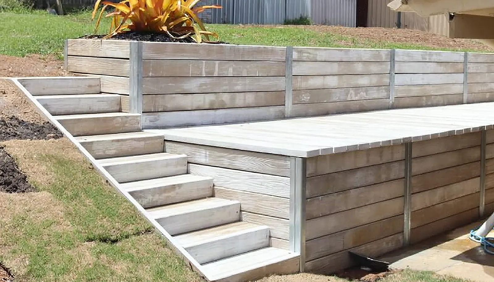 A pale grey Hybrid Sleeper retaining wall with built-in stairs on a sloping backyard
